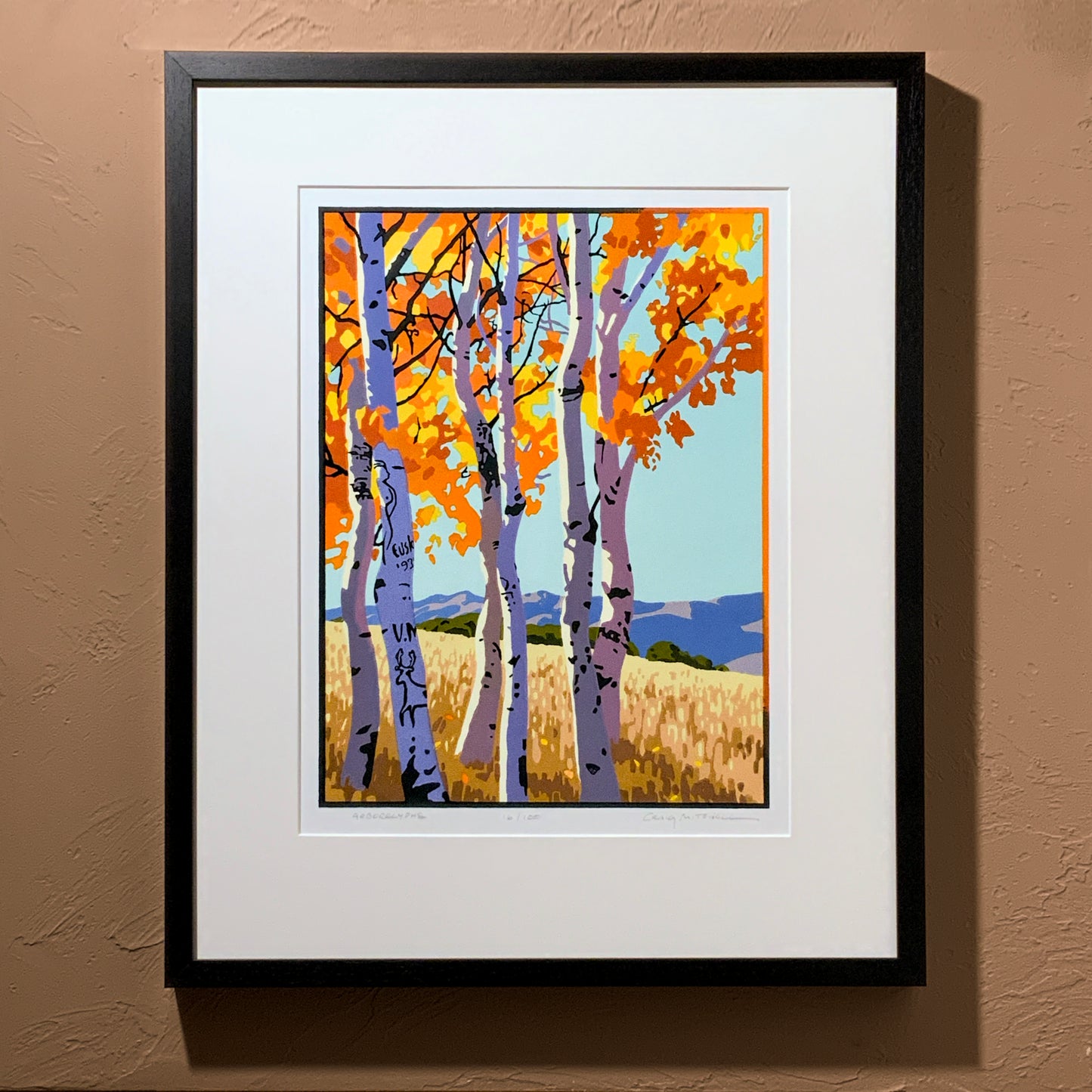 A framed art print depicting a grove of aspen trees with autumn-colored leaves and arboglyphs, displayed on a wall.