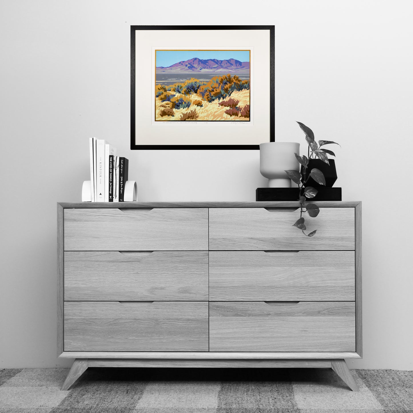 Gray dresser with framed artwork above it in a room setting.