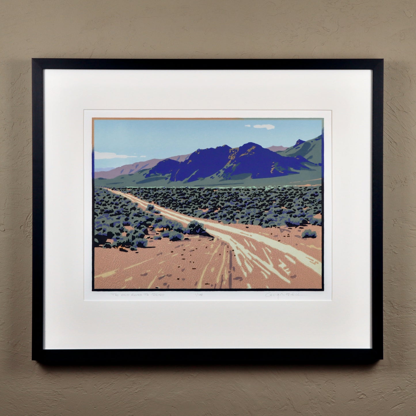 Framed artwork of a desert landscape with mountains on a beige wall.