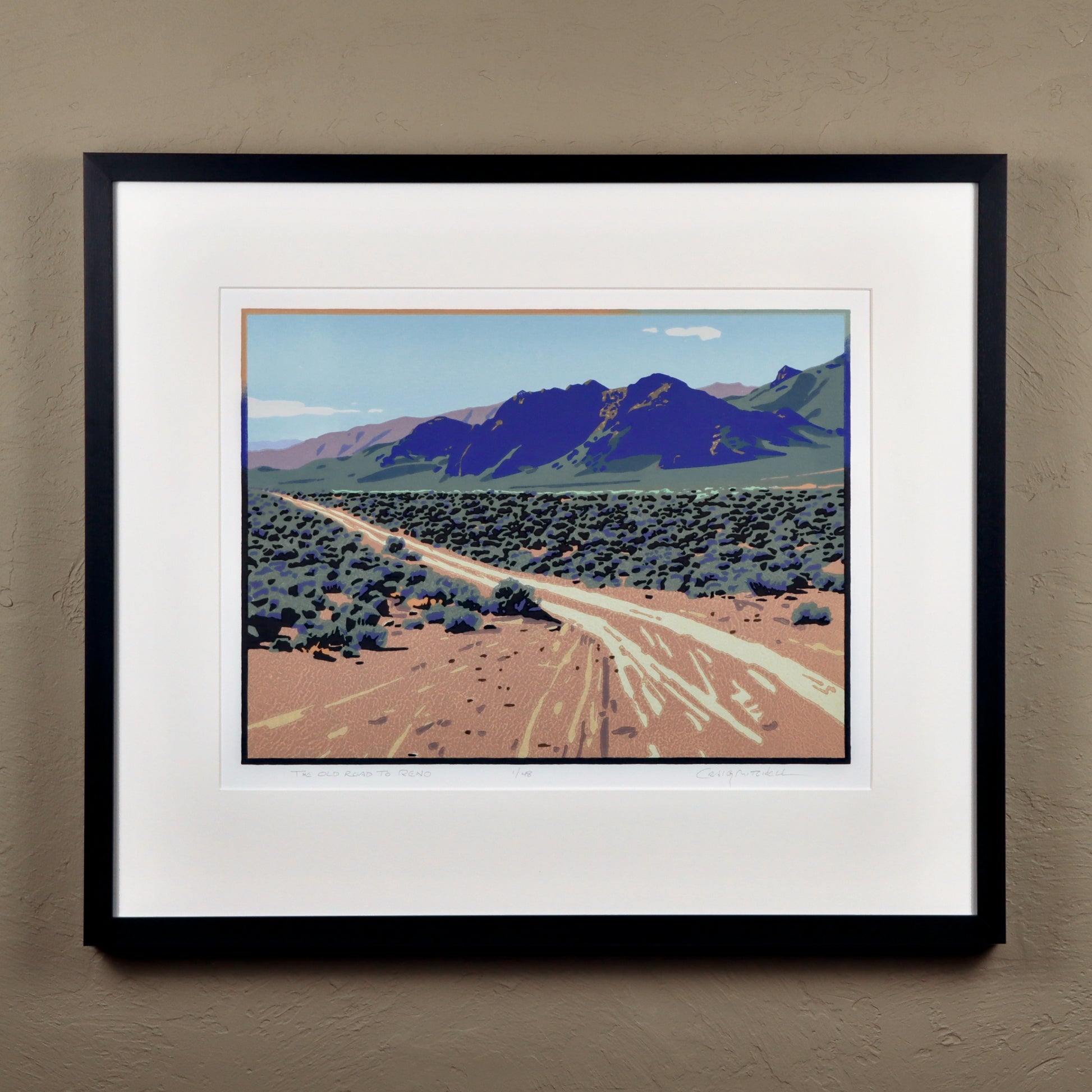 Framed artwork of a desert landscape with mountains on a beige wall.