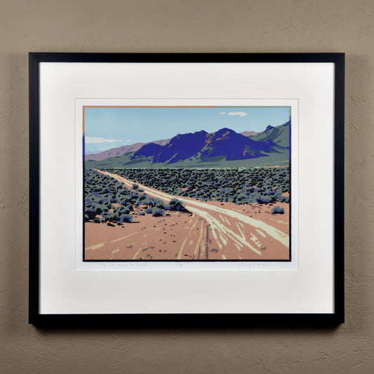 Framed artwork of a desert landscape with mountains on a beige wall.