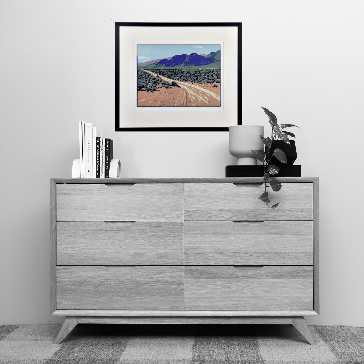 Gray dresser with decorative items including a framed landscape print on a white wall.