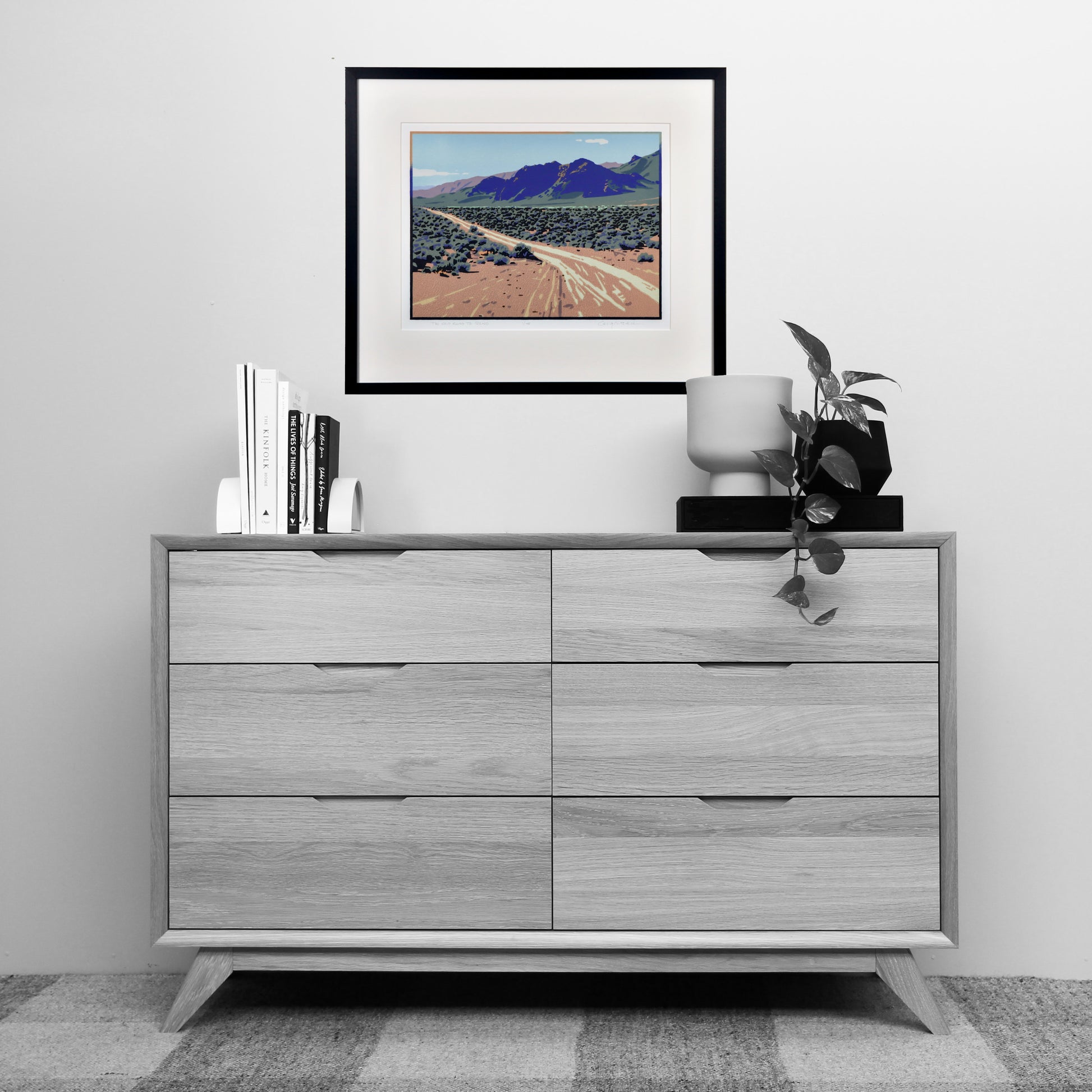 Gray dresser with decorative items including a framed landscape print on a white wall.