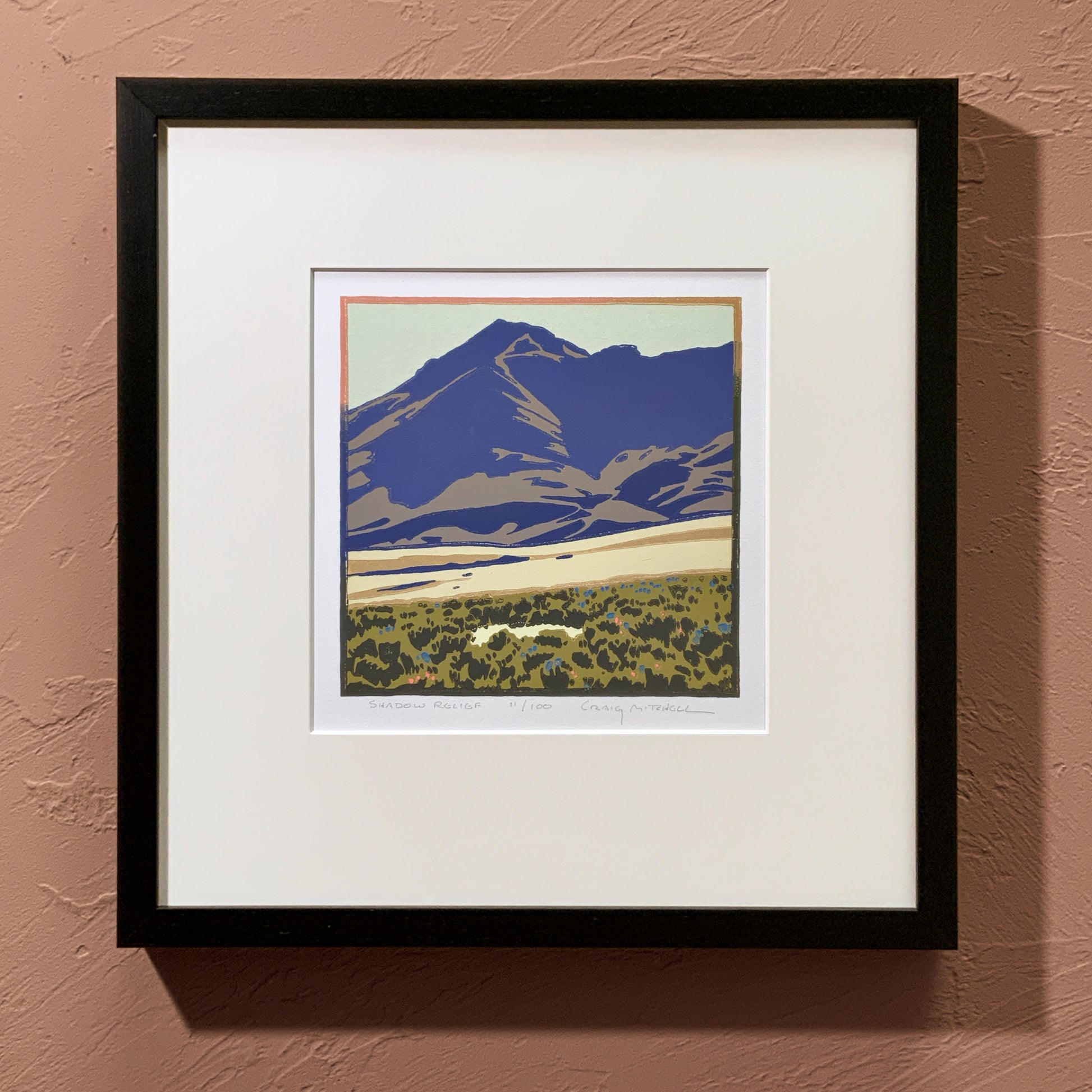 Framed artwork of a mountain landscape on a beige wall.