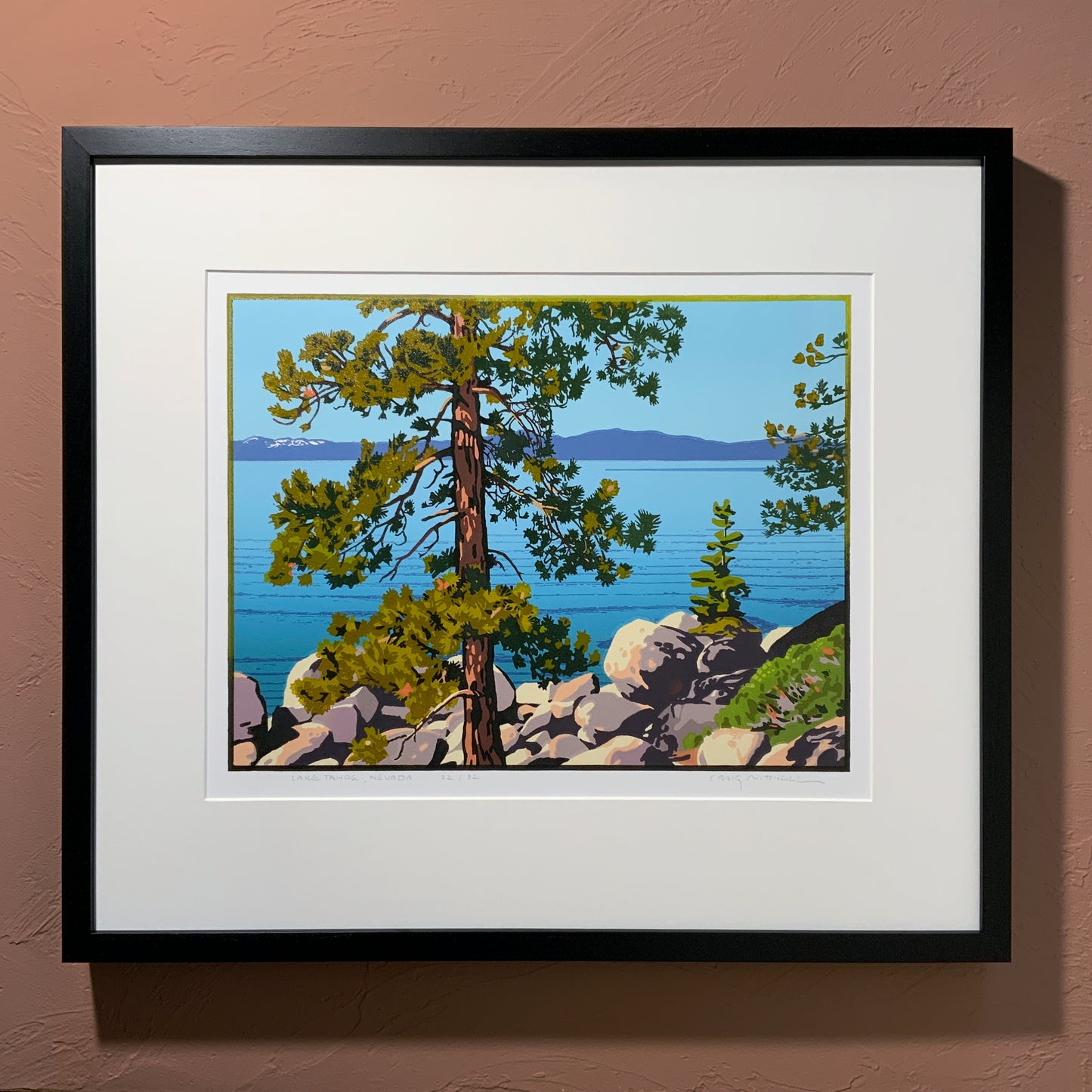 Framed artwork of a scenic Lake Tahoe landscape with trees and water on a brown wall.