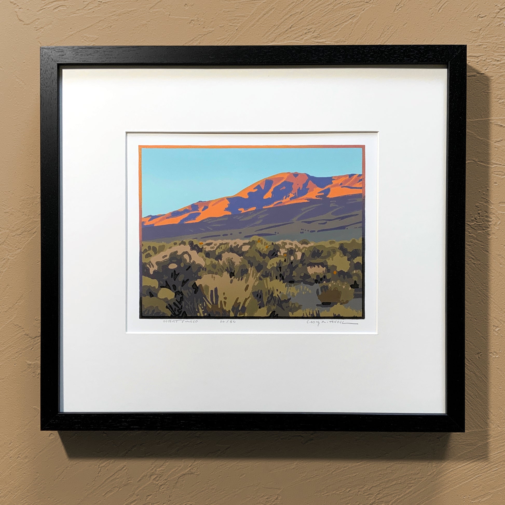 A framed art print titled 'Desert Finale' depicting a mountain landscape with a pink and orange sunset, set in a black frame.