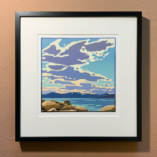 A framed art print depicting a scenic view of Lake Tahoe with clouds in the sky, placed against a neutral wall.