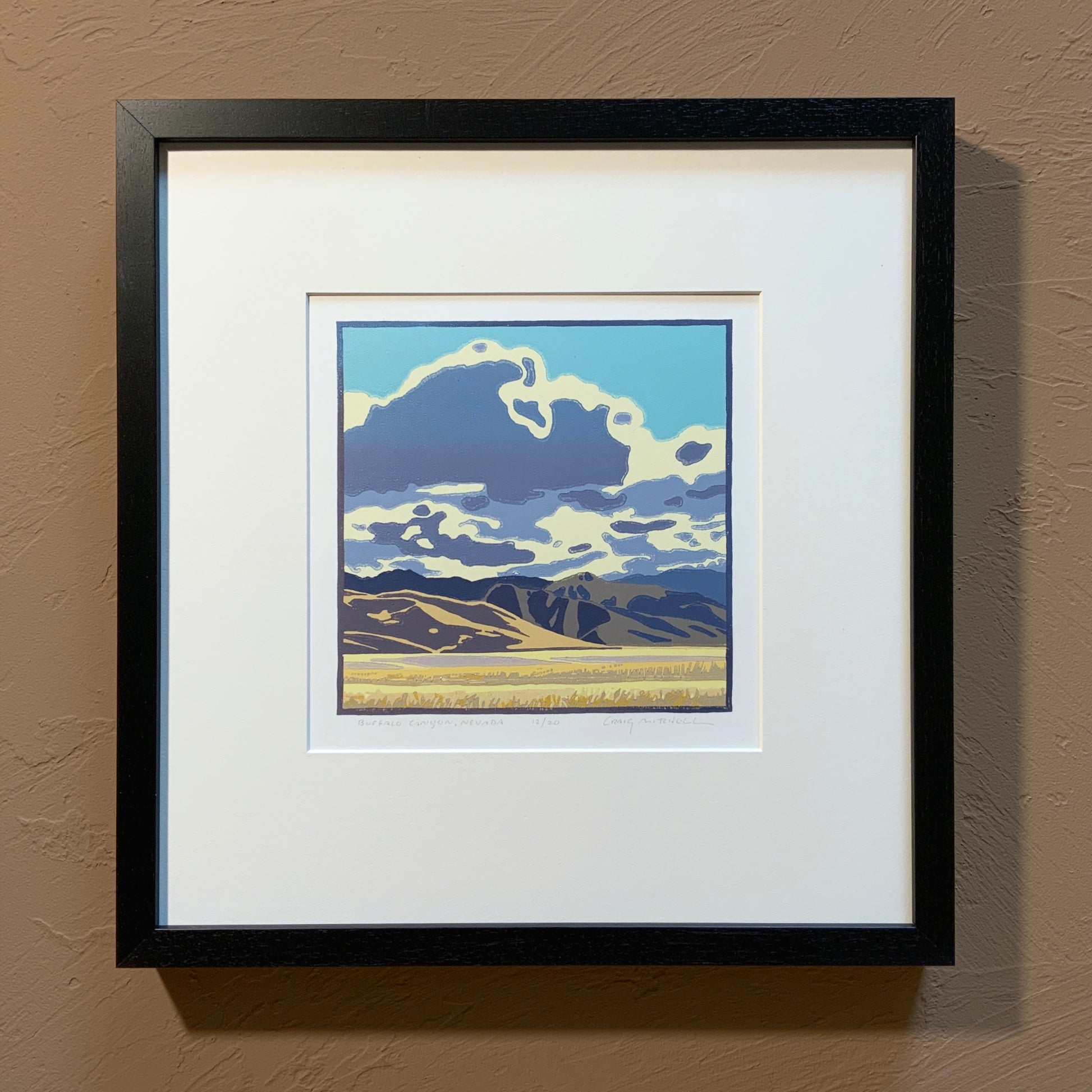 A framed artwork depicting a stylized landscape with clouds in the sky and mountains in the background, primarily in blue and white tones.