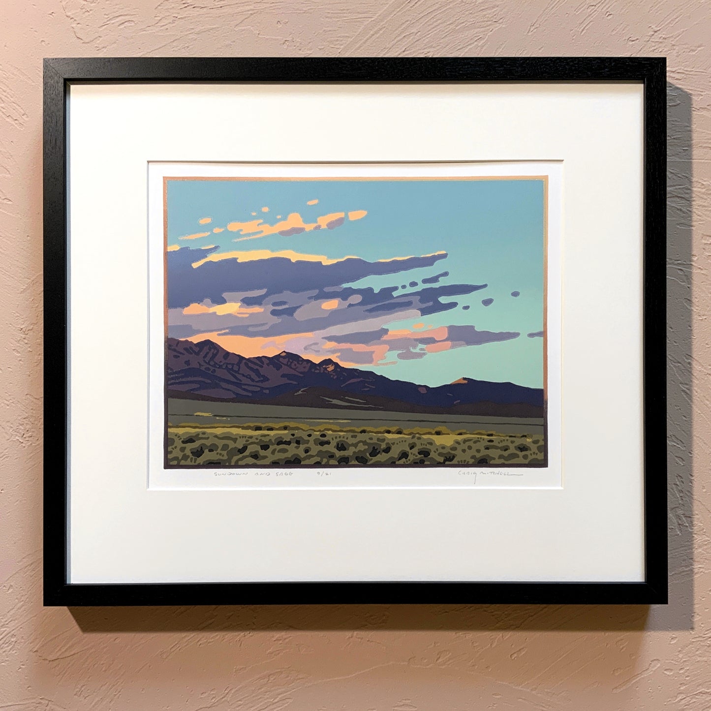A framed artwork called "Sundown and Sage" depicting a sunset over a mountain range, with a black frame and a white mat.