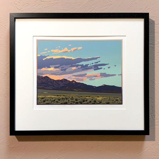 A framed artwork called "Sundown and Sage" depicting a sunset over a mountain range, with a black frame and a white mat.