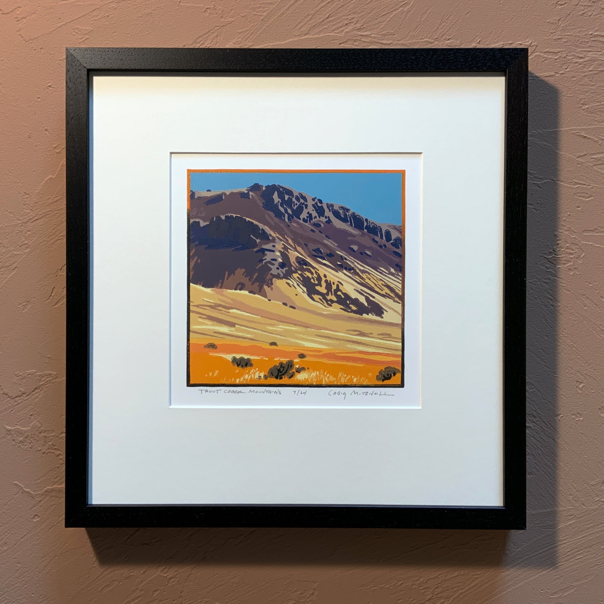 A framed artwork depicting a mountain range with a vibrant orange and brown color palette, titled 'Trout Creek Mountains'.